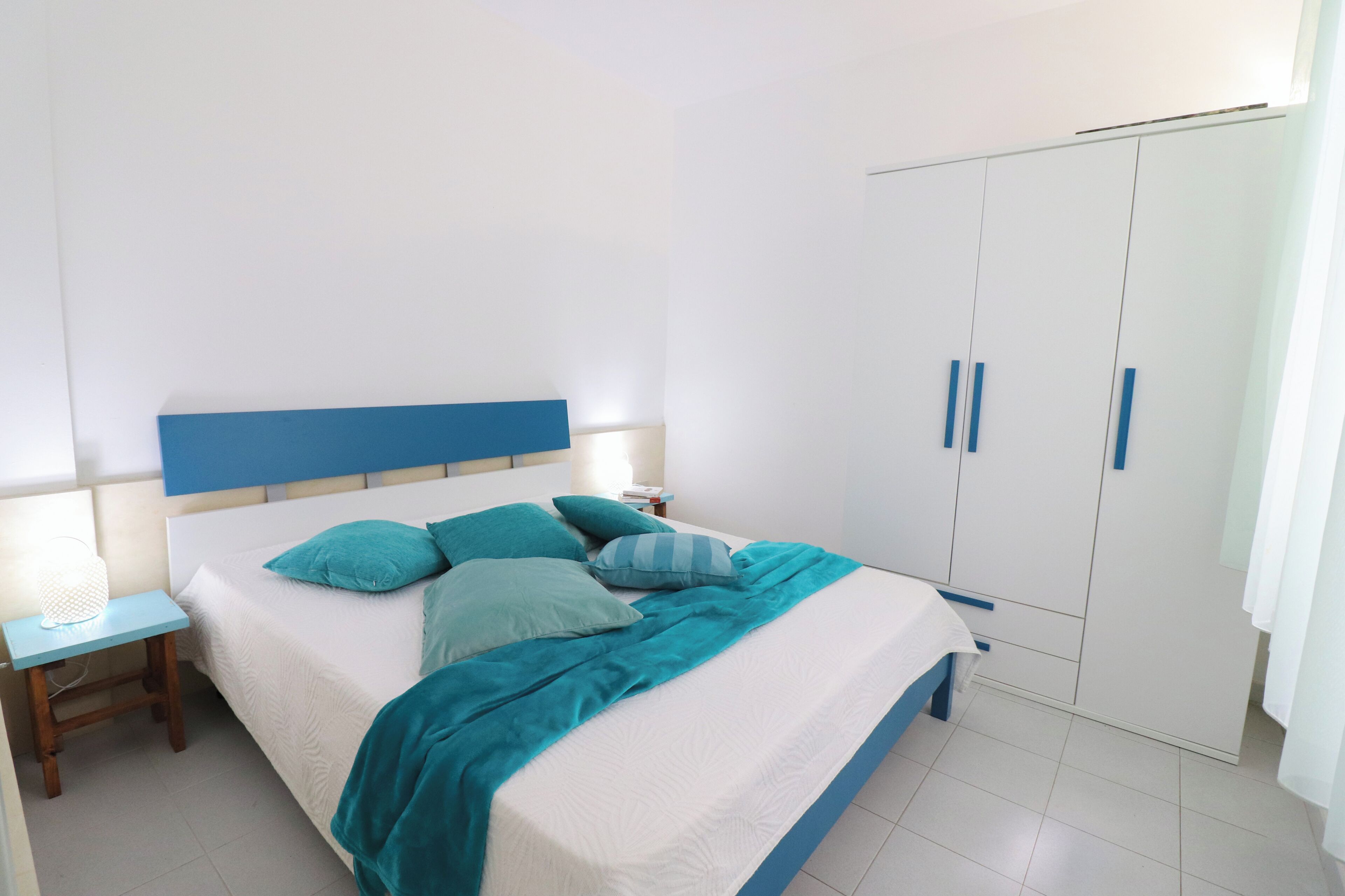 A bedroom with a bed, nightstand, wardrobe, and a bedside lamp.