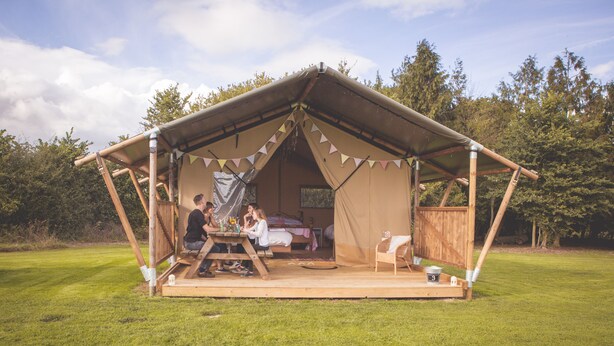 A tented outdoor accommodation with a picnic table, a bed, and a small seating area. - Canvas & Clover (Worcester)