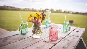 A wooden picnic table with four mason jars containing drinks, each with a straw. - Canvas & Clover (Worcester)