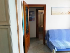 A room with a bed, a door, a bathroom, and a painting on the wall.