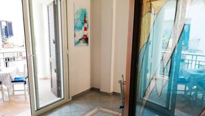 A room with a sliding glass door leading to a balcony, a small table with chairs, and a painting on the wall. - Holiday Home Barbara (Otranto)