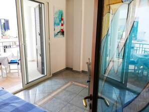 A room with a sliding glass door leading to a balcony, a small table with chairs, and a painting on the wall.