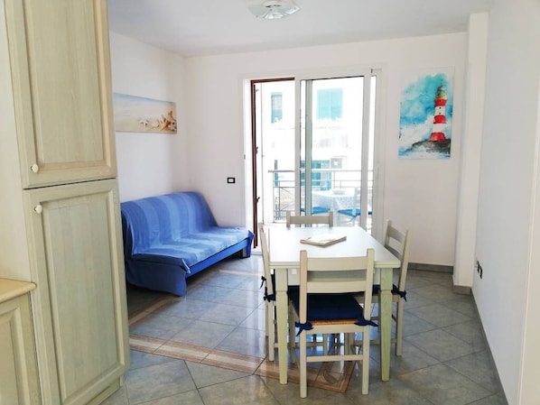 A room with a dining table, chairs, a blue sofa, a painting, and a view through a glass door.