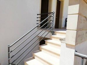 Un escalier avec des rampes en métal et des marches de couleur beige, menant à une porte intérieure.