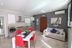A modern kitchen with white cabinets, a dining table with red chairs, and a white sofa in a living area. - Modern Apartment "casa Giuditta Deluxe A Otranto" (Otranto)