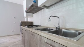 A modern kitchen with two stainless steel sinks, a gas stove, and wooden cabinets. - Modern Apartment "casa Giuditta Deluxe A Otranto" (Otranto)