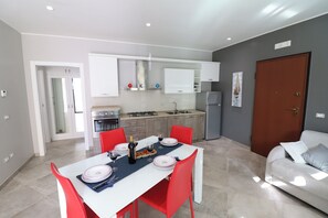 A modern kitchen with white cabinets, a dining table with red chairs, and a grey sofa in a living area. - Modern Apartment "casa Giuditta Deluxe A Otranto" (Otranto)
