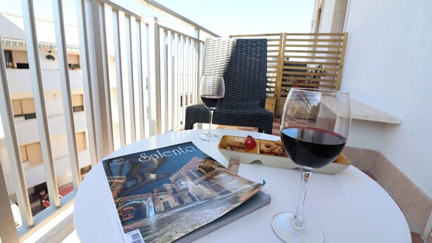 A table with a magazine, a glass of red wine, and a small dish with food on a balcony.