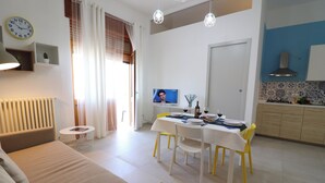 A modern living room with a sofa, a dining table with chairs, a TV, and a kitchen area with cabinets and a stove.