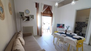 A living room with a beige sofa, a dining table set for four, and a television on the wall.