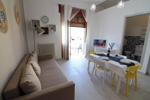 A living room with a beige sofa, a dining table set for four, and a television on the wall. - Casa Nike Comfort & Relax in the Heart of Otranto (Otranto)