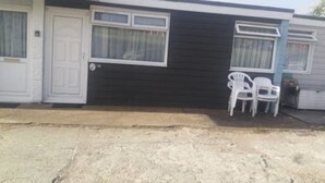 A single-story mobile home with a dark exterior, a white door, and a small porch area with two white plastic chairs. - 2 Bedroom Chalet Near the Beach (Sandown)