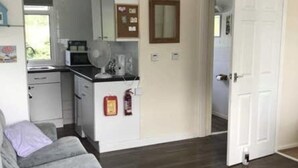A compact living space with a kitchenette, a grey sofa, and a wooden floor. - 2 Bedroom Chalet Near the Beach (Sandown)