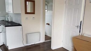 A compact living space with a kitchenette, a dining area, and a door leading to another room. - 2 Bedroom Chalet Near the Beach (Sandown)