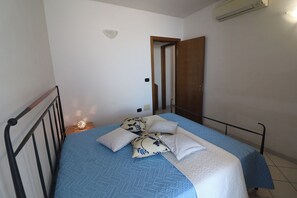 Ein Schlafzimmer mit einem Einzelbett, einem Nachttisch mit Lampe und einer Tür zu einem anderen Raum.