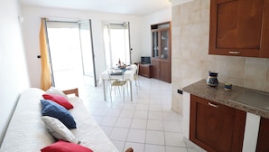 A modern kitchen with granite countertops and wooden cabinets, a dining area with a table and chairs, and a living area with a sofa and cushions. - Casa Vanessa Modern One-bedroom Apartment With sea View in Central Otranto (Otranto)