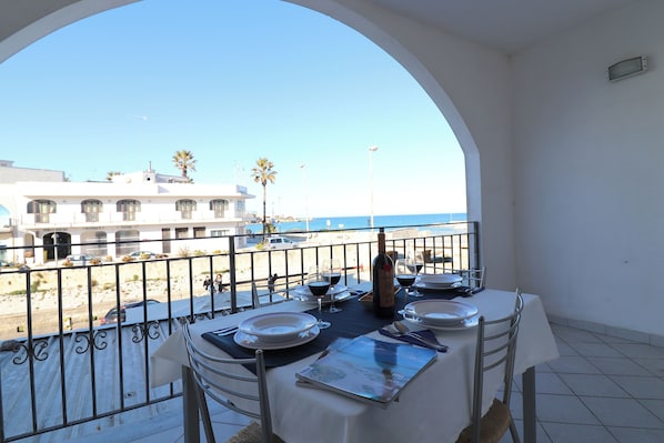 Une table installée sur un balcon, prête pour un repas, avec vue sur la plage et les bâtiments.