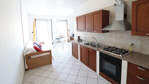 A kitchen with wooden cabinets, a gas stove, a sink, and a tiled floor. - Casa Vanessa Modern One-bedroom Apartment With sea View in Central Otranto (Otranto)