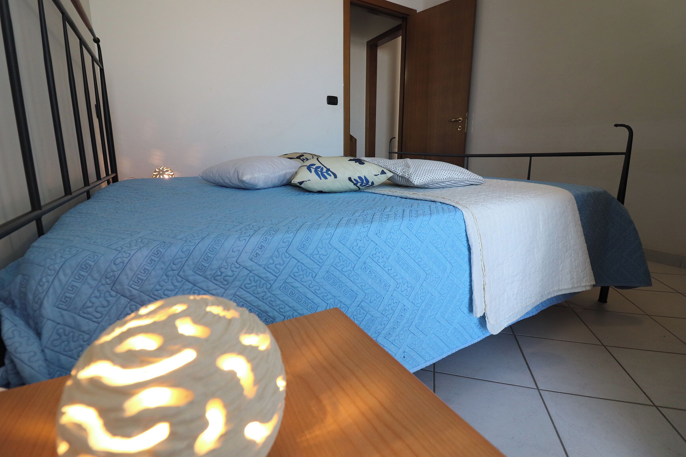 Een slaapkamer met een bed, kussens, een nachtkastje en een bedtafel.
