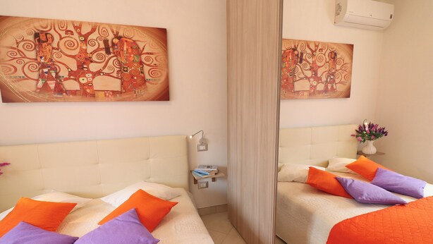 Una habitació d'hotel amb dos llits, cadascun amb roba de llit taronja i morada, un mirall gran i dos quadres penjats a la paret.