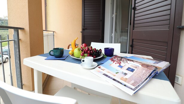 A balcony with a table set with a plate of fruit, a white cup, and a magazine. - Holiday's Home Claudia 6 People (Otranto)