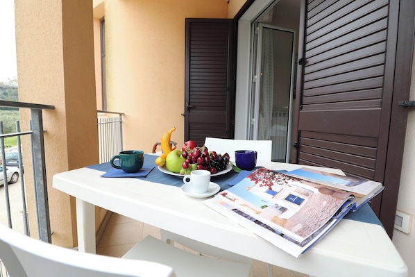 En balkong med ett bord dukat för frukost, med frukt, en kopp och en tidning.