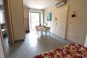 Et hotelværelse med seng, spisebord med stole, et billede på væggen og en aircondition.