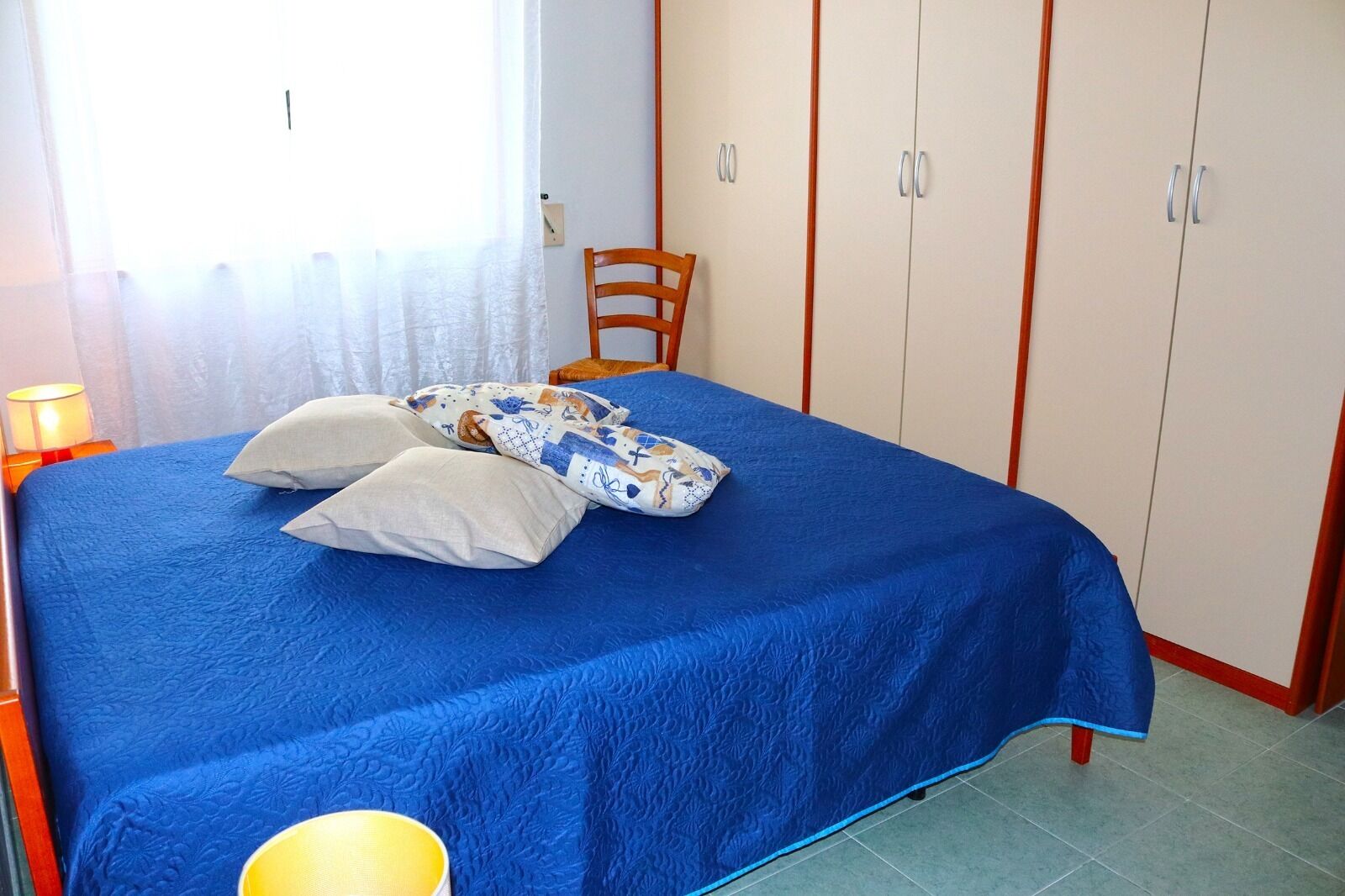 A bedroom with a bed, pillows, a chair, and a wardrobe.