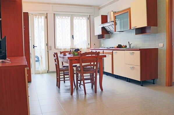 A compact kitchen with a dining table and chairs, a built-in oven, and a window with curtains.