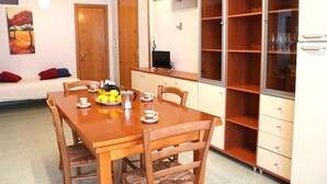A dining area with a wooden table, chairs, and a fruit bowl. There is a bed with red and blue pillows in the background. - Holiday Apartment Karm Otranto 6 Places (Otranto)