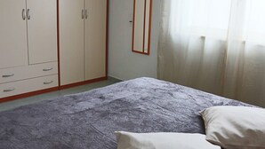 A bedroom with a bed, a wardrobe, and a window with curtains. - Holiday Apartment Karm Otranto 6 Places (Otranto)