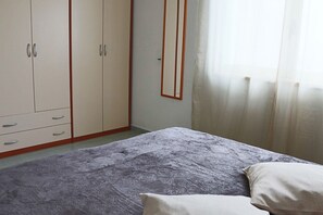 A bedroom with a bed, a wardrobe, and a window with curtains. - Holiday Apartment Karm Otranto 6 Places (Otranto)