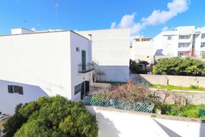 Un bâtiment blanc doté d’un balcon, entouré de verdure et d’une clôture.