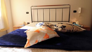 Ein Bett mit Metallkopfteil, mehreren Kissen, einer Decke und einem Nachttisch mit Lampe und Dekorationsobjekt.