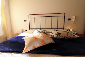 A bed with a metal headboard, multiple pillows, a bedside table with a lamp, and a wall-mounted phone.