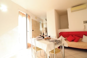 A dining area with a table set for four, a red sofa, and a kitchen in the background.