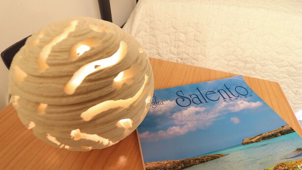 Ein runder, strukturierter Gegenstand auf einer Holztischplatte neben einer Broschüre mit dem Titel „Salento Review“ und einem Bild von einer Küstenlandschaft.