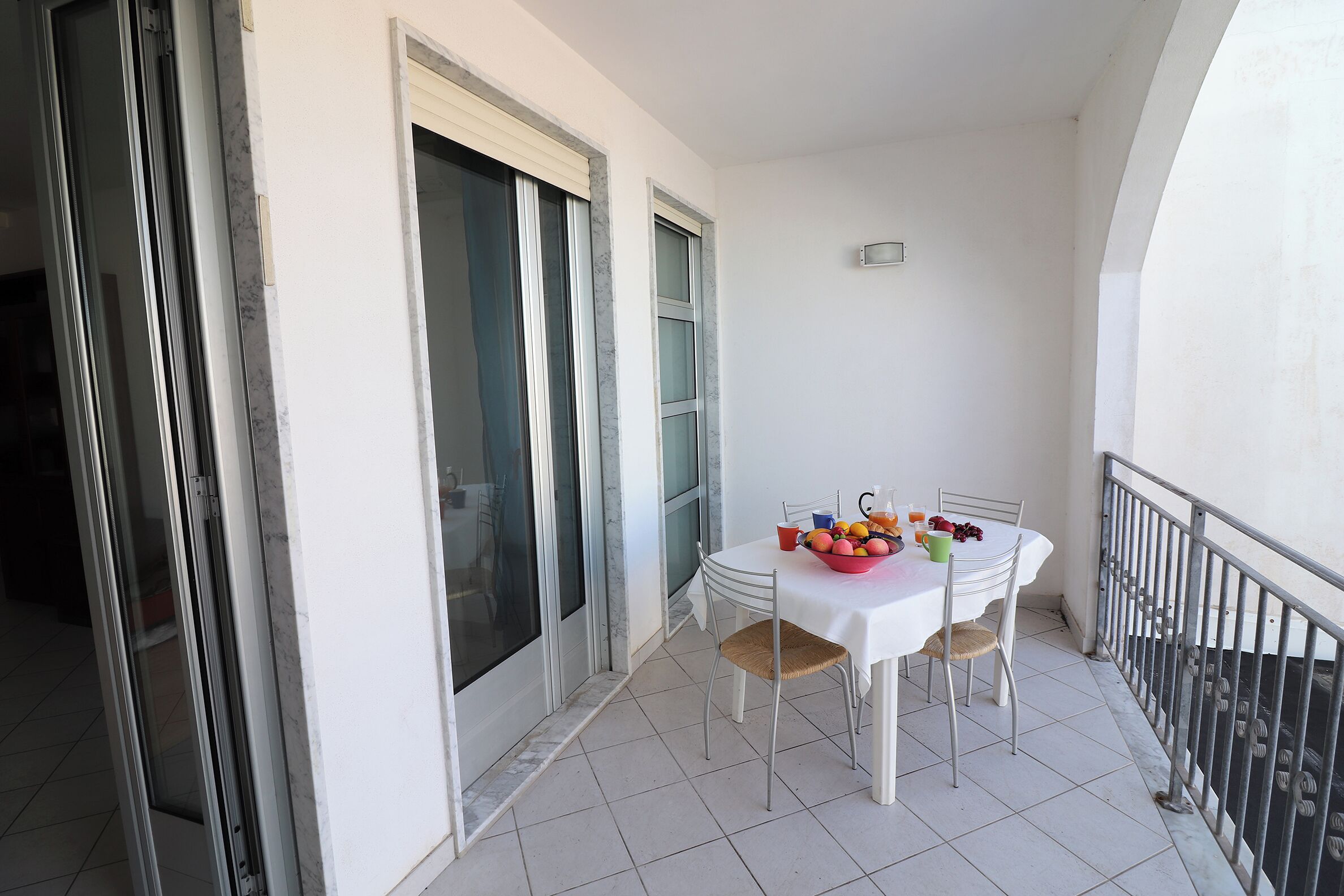 A balcony with a white table, chairs, and a fruit bowl.
