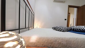 A bedroom with a bed, a wooden nightstand, a patterned pillow, and a door leading to another room. - Holiday Home "arianna" Elegance and Comfort in the Heart of Otranto (Otranto)
