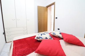 Une chambre à coucher avec un lit, des oreillers rouges, une armoire blanche et une porte en bois.