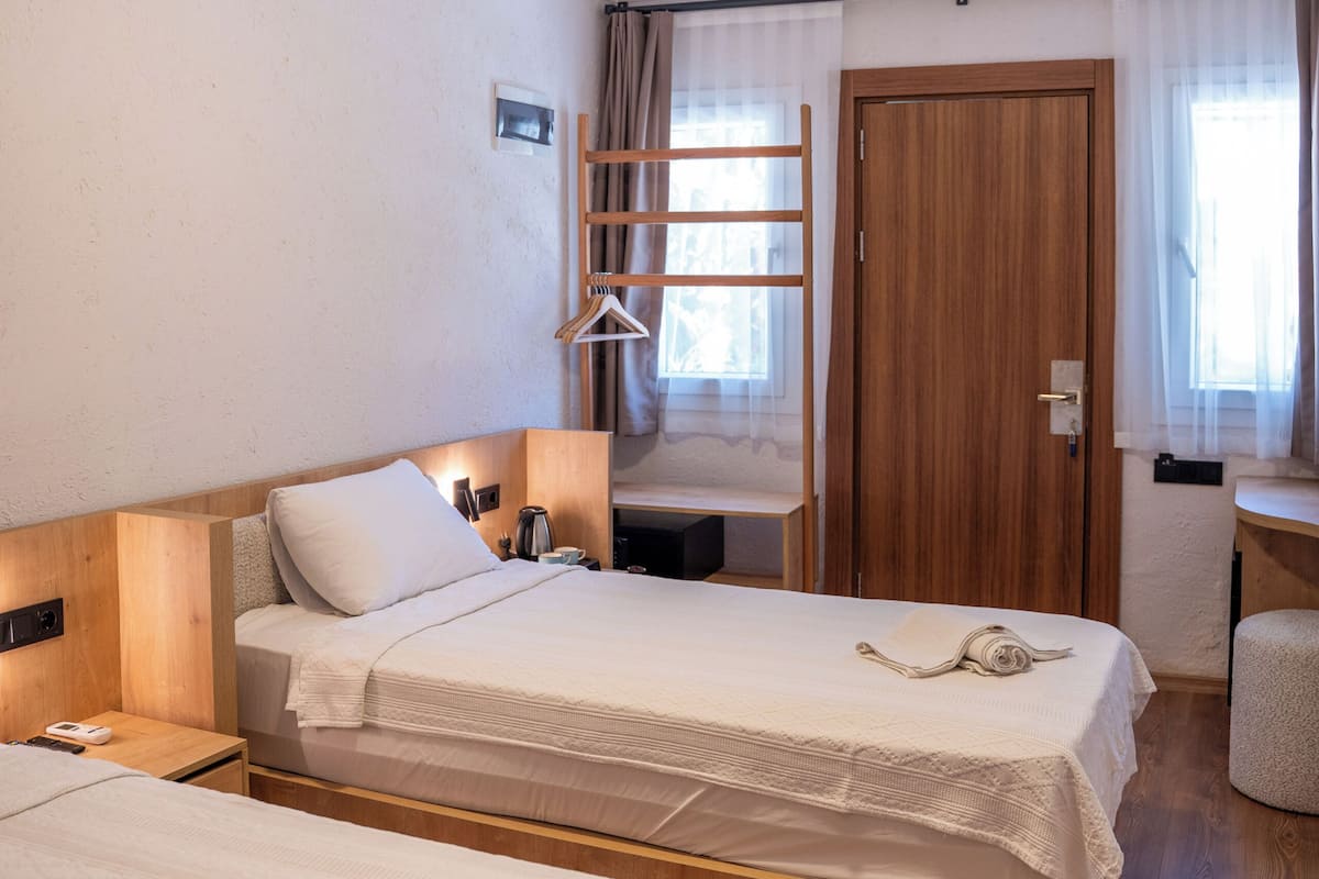 Une chambre d’hôtel avec deux lits, une armoire en bois, un bureau avec une chaise et une fenêtre avec des rideaux.