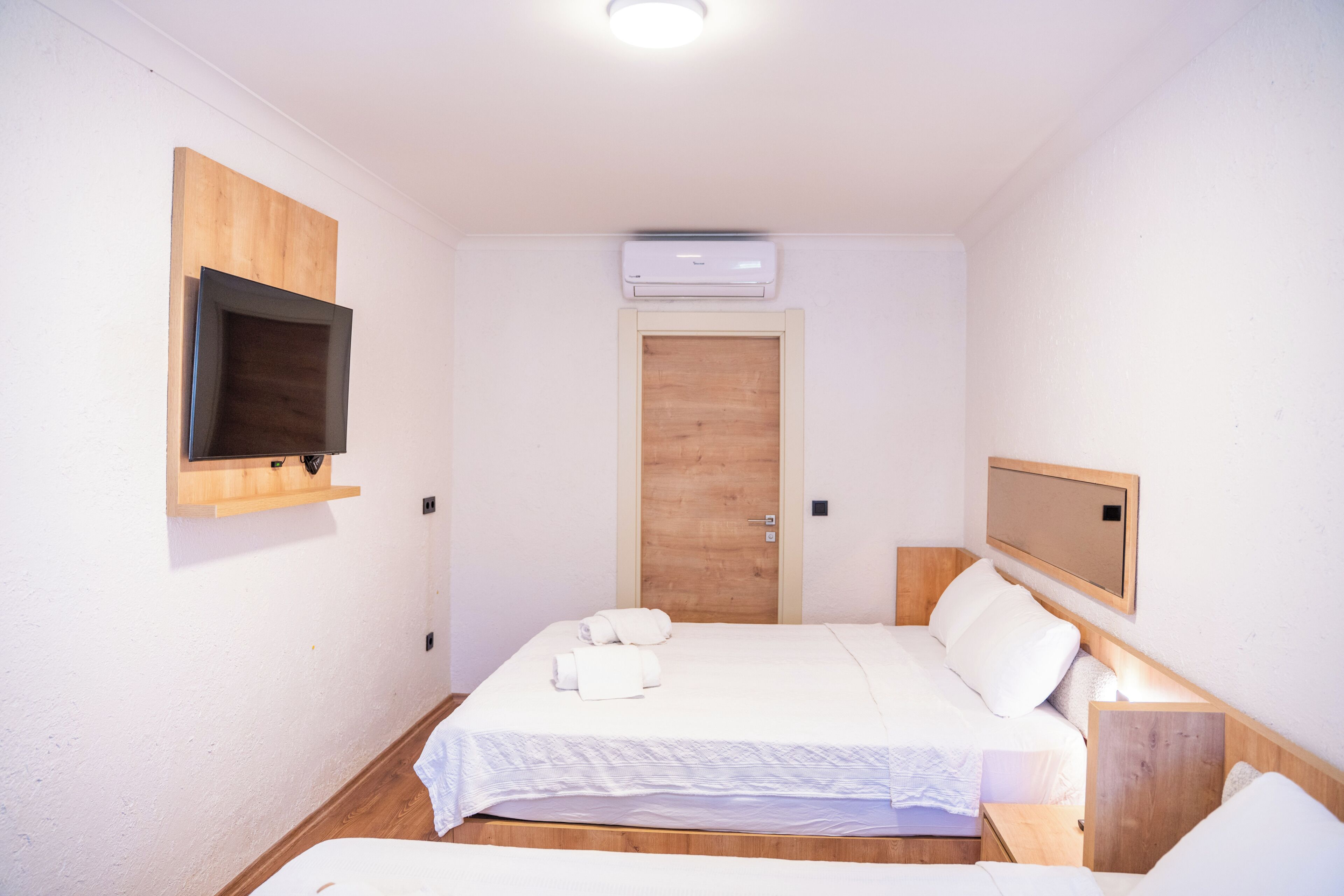 A small, clean room with a bed, a mounted TV, and an air conditioning unit.
