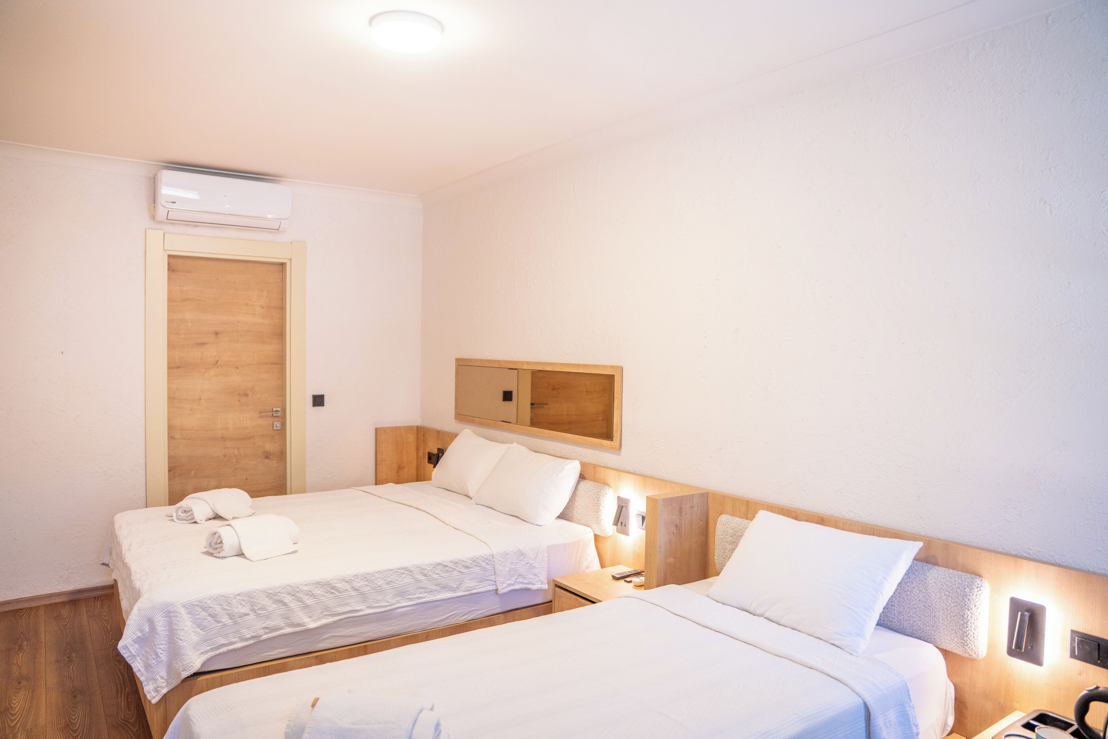 A hotel room with two beds, a wooden door, a mirror, and a wall-mounted air conditioner.
