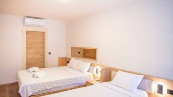 A hotel room with two beds, a wooden door, a mirror, and a wall-mounted air conditioner.