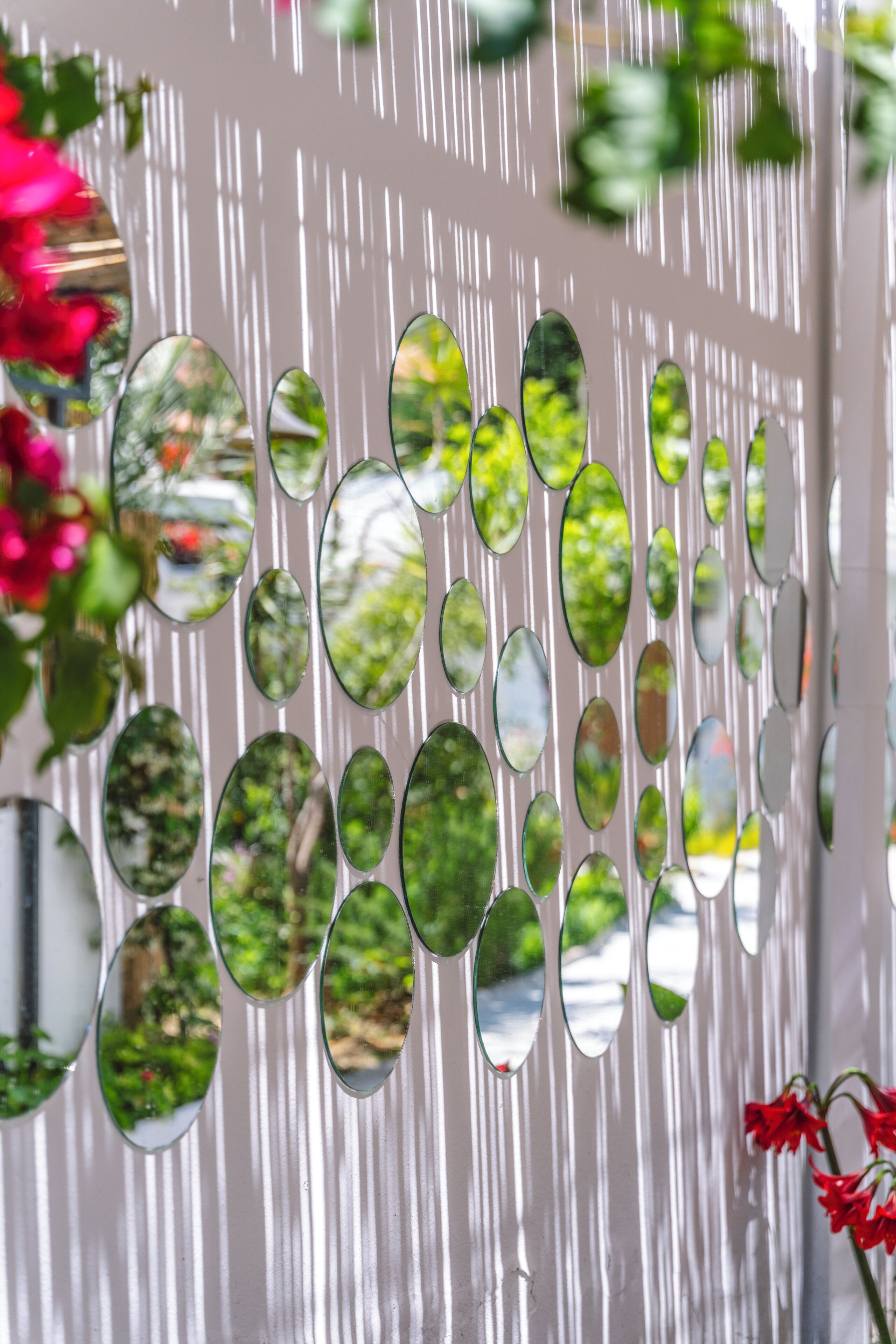 A wall with multiple oval mirrors reflecting greenery.