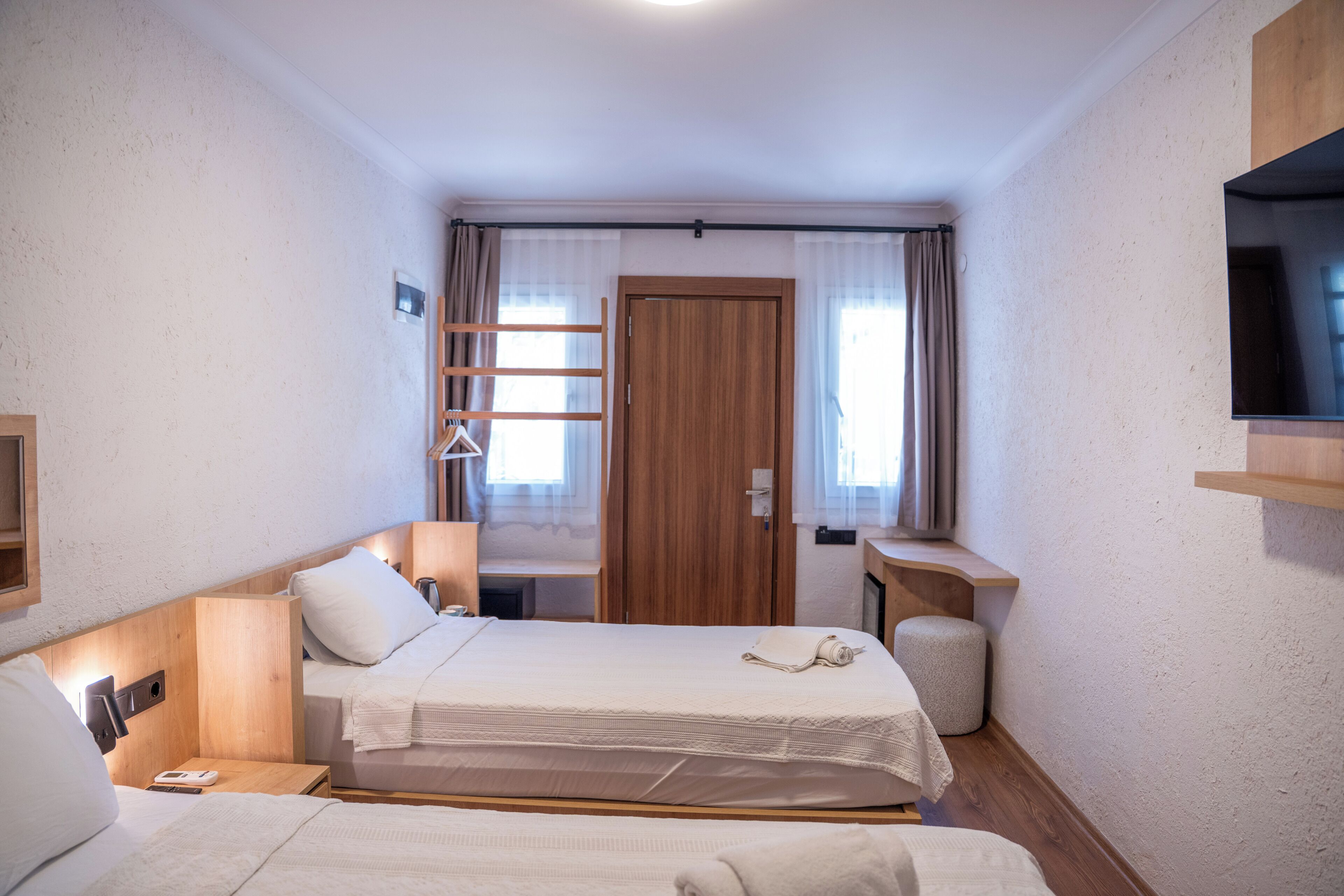 Een hotelkamer met twee bedden, een houten garderobe, een televisie en een klein tafeltje.