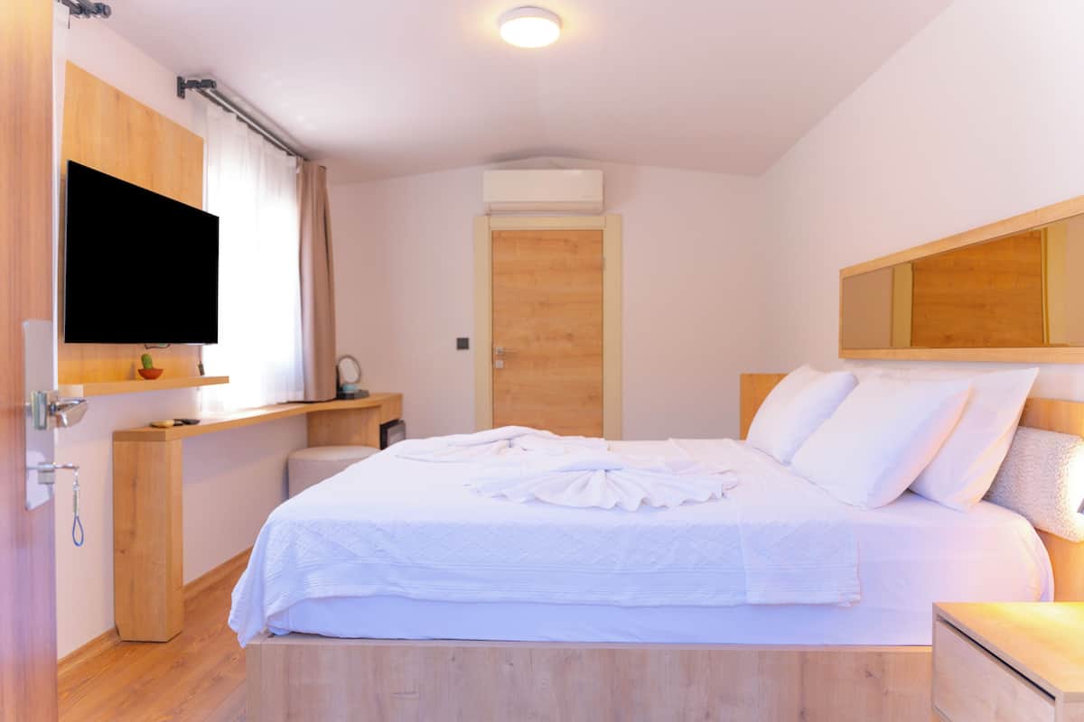 Une chambre à coucher avec un lit, une tête de lit en bois, un téléviseur fixé au mur et une porte.