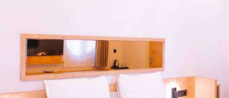 A hotel room with a bed, a bedside table, a nightstand, a wall-mounted TV, and a mirror.