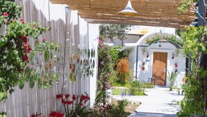 Un sendero que lleva a un edificio con puerta de madera, rodeado por un jardín con diversas plantas y flores.