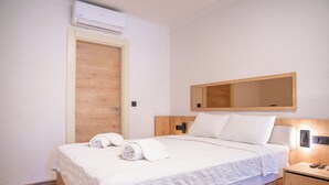 Habitación de hotel con una cama de madera, una mesita de noche con lámpara, un espejo en la pared y un equipo de aire acondicionado.